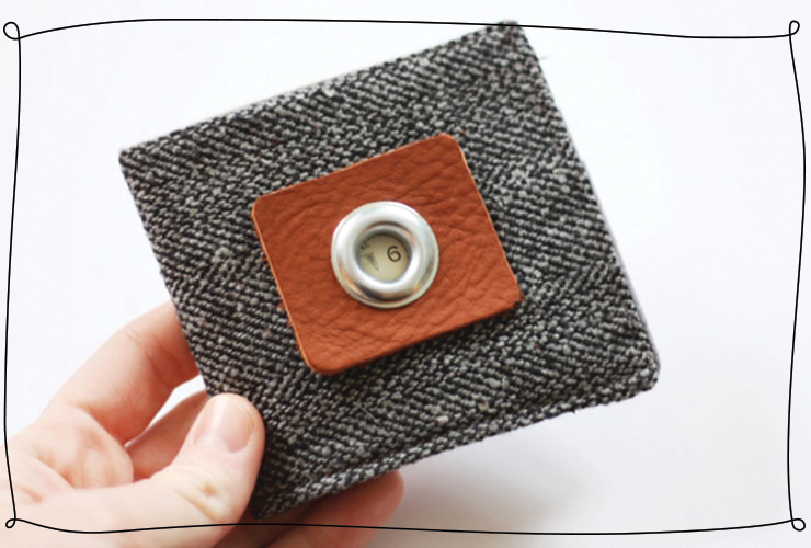 Hand holding a simple gray wallet with a brown accent square on it